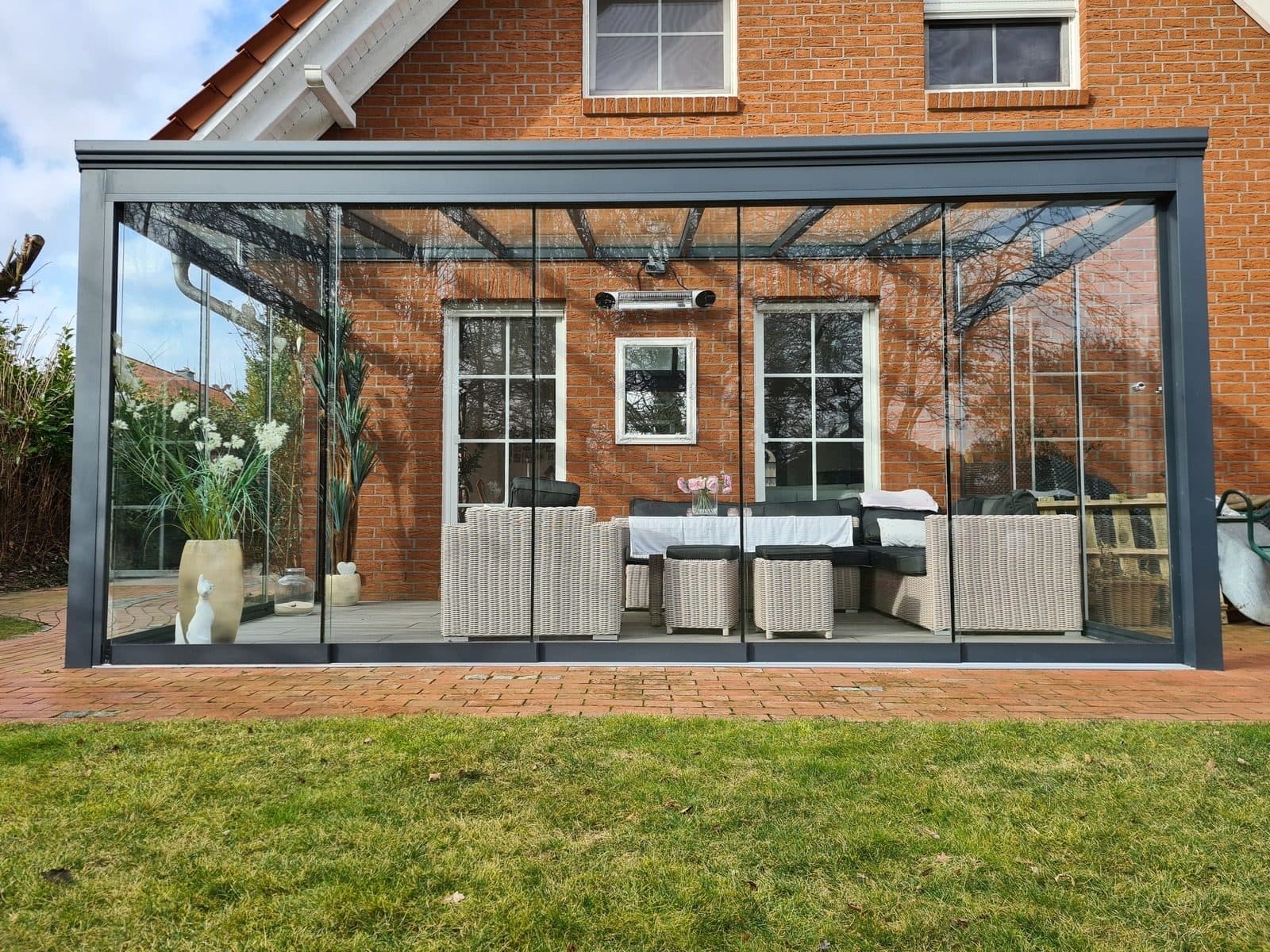 Gebauter Kaltwintergarten an einem Klinkerhaus, rundum verglast, mit Sitzgruppe darin